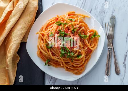 Italiano autentico bucatini all'amatriciana fatta con pomodori san marzano e guarnita con un fresco e basilico tritato e scorza di formaggio pecorino romano Foto Stock