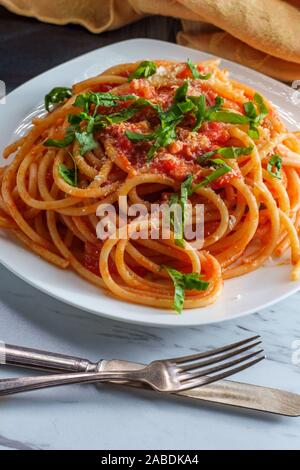 Italiano autentico bucatini all'amatriciana fatta con pomodori san marzano e guarnita con un fresco e basilico tritato e scorza di formaggio pecorino romano Foto Stock