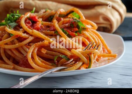 Italiano autentico bucatini all'amatriciana fatta con pomodori san marzano e guarnita con un fresco e basilico tritato e scorza di formaggio pecorino romano Foto Stock