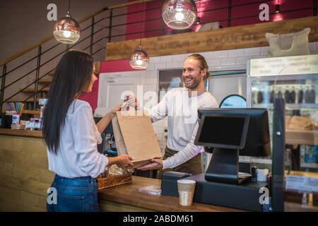 Dai capelli scuri imprenditrice parlando al cassiere sorridente nel coffee shop Foto Stock