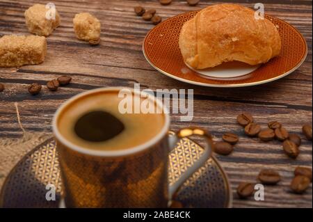 Tazza da caffè, croissant, lo zucchero di canna e i chicchi di caffè su sfondo di legno. Close up Foto Stock