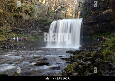 Persone turisti guardando Sgwd yr Eira sulla cascata Afon Mellte Fiume Ystradfellte Pontneddfechan Parco Nazionale di Brecon Beacons Fforest Fawr Geopark Foto Stock