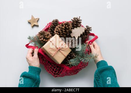 Donna mani tenendo borsa a rete con Natale rifiuti zero decor, dono sostenibile, coni e Abete rami per design fatti a mano. Eco Friendly Xmas. Foto Stock