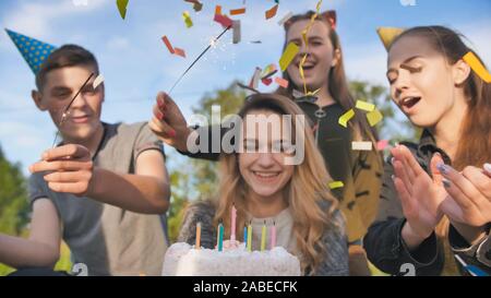 Happy amici celebrano la loro ragazza il compleanno. La ragazza di compleanno si brucia le candele. Foto Stock