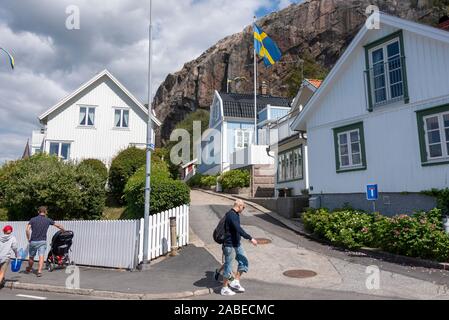 09 luglio 2019, Svezia, Fjällbacka: i turisti a piedi attraverso Fjällbacka. Di fronte a una casa la bandiera svedese si brucia. Fjällbacka è una rinomata località di villeggiatura sulla svedese costa ovest. Foto: Stephan Schulz/dpa-Zentralbild/ZB Foto Stock