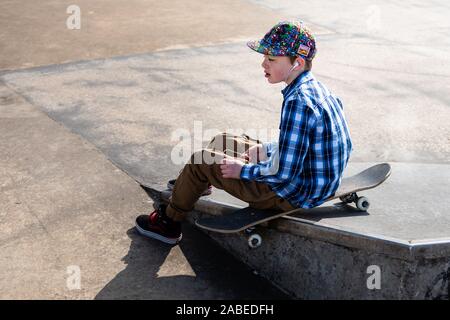 Un grazioso piccolo ragazzo con sindrome di Asperger, ADHD, autismo equitazione intorno al skatepark ascolto di musica e la pratica di trucchi, scendere una scalinata, Ollie etc Foto Stock