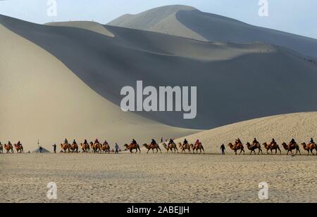 Gruppi di turisti corsa cammelli si muovono su cantando le dune di sabbia in Dunhuang, una contea-livello città di Jiuquan city, a nord-ovest della Cina di provincia di Gansu, 14 ott Foto Stock