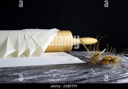 Primo piano di pasta fillo su un tavolo infarinato. Sfondo scuro con il mattarello e spighe di grano. Foto Stock