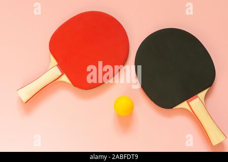 Nero e rosso tennis ping pong racchette e sfera arancione isolata su uno sfondo rosa, attrezzature sportive per il tennis da tavolo Foto Stock