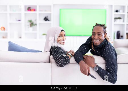 African giovane seduto sul divano guardando la TV insieme Chroma schermo verde donna che indossa il Hijab islamico vestiti Foto Stock