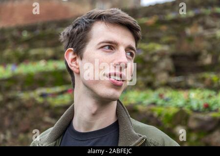 Un bel giovane uomo nel suo late adolescenti o poco più che ventenne sorge all'aperto e sorrisi come egli guarda al lato. Foto Stock