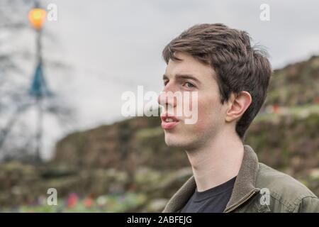 Un giovane uomo nel suo late adolescenti o poco più che ventenne sorge all aperto con un pensieroso espressione come egli appare in lontananza. Foto Stock