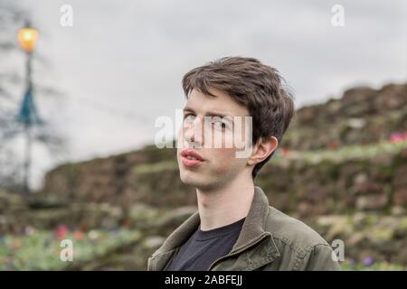 Un giovane uomo nel suo late adolescenti o poco più che ventenne guarda questioningly presso la telecamera come se scettico. Foto Stock