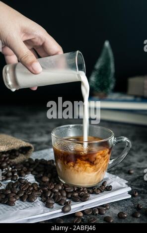 Barista rendendo il latte. mano versando il latte in una tazza di caffè espresso, preparazione di bere caffè. L'immagine verticale, ritagliato shot Foto Stock