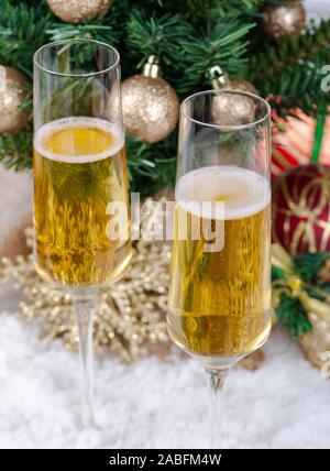 Primo piano di due bicchieri di champagne con albero di Natale decorato in background sulla neve Foto Stock