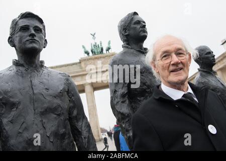 Berlino, Germania. 27 Nov, 2019. John Shipton, padre di incarcerati Wikileaks fondatore J. Assange, sorge di fronte alla Porta di Brandeburgo a una manifestazione per la libertà di J. Assange nella parte anteriore di una scultura in bronzo che mostra Assange (M) e Chelsea Manning. Assange è in carcere a Londra e mostra segni di "torture psicologiche' secondo il relatore speciale delle Nazioni Unite. Gli Stati Uniti hanno presentato una richiesta di estradizione, dove egli è minacciato con 175 anni di reclusione. Credito: Jörg Carstensen/dpa/Alamy Live News Foto Stock