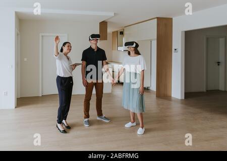 Agenti immobiliari con coppia giovane che indossa gli auricolari VR nel nuovo appartamento Foto Stock