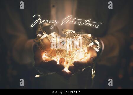Merry Christmas greeting card - le luci a led garland incandescente nella mani della donna Foto Stock