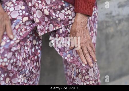 Le mani di una vecchia donna in abiti luminosi seduta su un parapetto di pietra Foto Stock