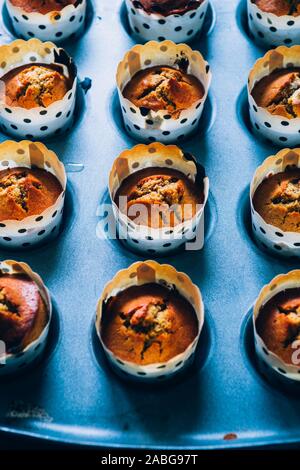 In prossimità di alcuni appena sfornato di zucca muffin rivestiti su un alluminio vassoio da forno per la Festa di halloween visualizzata su un blu scheda rustico, laici piatta vista dall'alto,nat Foto Stock