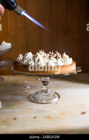 Crostata al limone con meringa francese caramellato sulla parte superiore, su un tavolo rustico, francese meringa caramellato con una torcia di cibo. Foto Stock