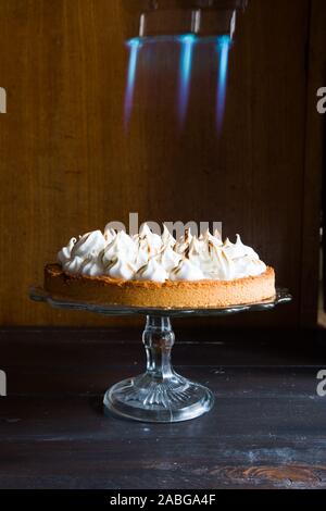 Crostata al limone con meringa francese caramellato sulla parte superiore, su un tavolo rustico, francese meringa caramellato con una torcia di cibo. Foto Stock