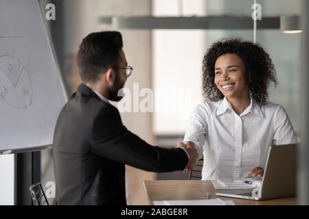 Sorridente biracial imprenditrice handshake collega di sesso maschile a briefing Foto Stock