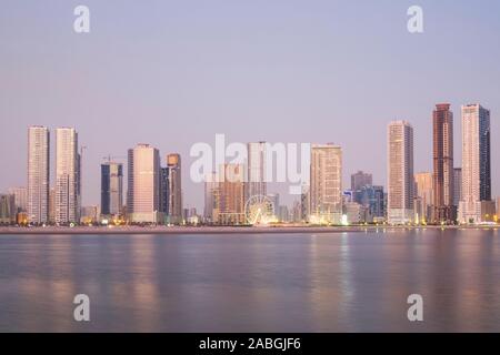 Crepuscolo vista dello skyline di spiaggia e alto e moderno appartamento edifici lungo la corniche in Sharjah Emirati Arabi Uniti Foto Stock