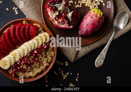 Dieta sana prima colazione concetto. Porridge di avena con banana, i semi di melograno e opuntia cactus di frutta. Copia dello spazio. Il sovraccarico laici piatta Foto Stock