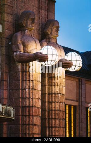 Helsinki, Finlandia. Vista notturna di due coppie di statue tenendo le lampade sferiche su ingresso a Helsinki la Stazione Ferroviaria Centrale. Di sera o di notte Il Foto Stock