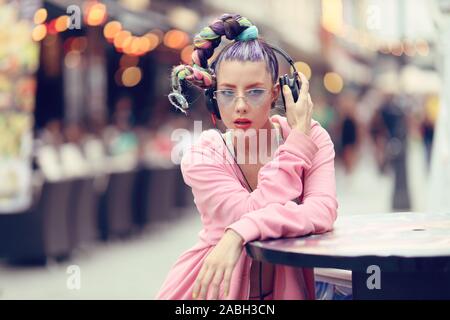 Giovane donna ascoltando la musica attraverso le cuffie sulla strada - Hipster Ragazza con un nonconformista cerca di moda Foto Stock