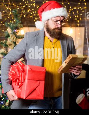 Uomo Barbuto hipster usura santa hat tenere mazzetto di lettere e confezione regalo. Uomo Barbuto con occhiali lettura posta per santa. Spirito di miracolo d'inverno. Post per babbo natale. Lettera a Babbo Natale. Foto Stock