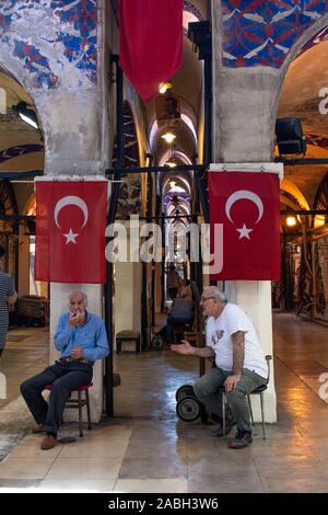 Istanbul: Turco uomini posti a sedere e parlare sotto due bandiere turche entro il Grand Bazaar, uno dei più grandi e più antiche mercati coperti in tutto il mondo Foto Stock