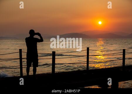 Silhouette di uomo che scattare una foto del tramonto sul suo telefono cellulare. Foto Stock