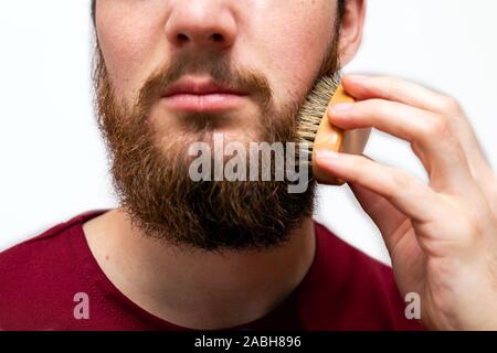 Primo piano di uomo bello spazzolando la sua barba su sfondo bianco isolato Foto Stock