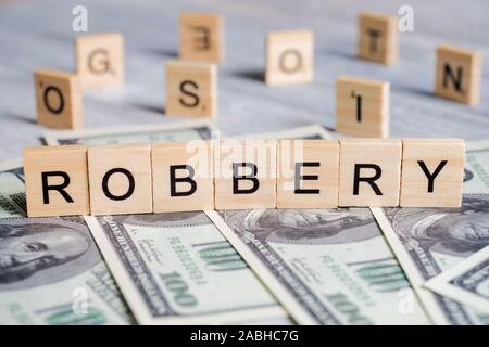 Parola fatta di lettere in legno - rapina, su uno sfondo grigio con dollari USA. Il concetto di infrangere la legge. Close up. Foto Stock