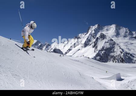 Sci freestyle con ponticello attraversato gli sci contro montagne innevate e cielo blu a sun giorno d'inverno. Lo Snowpark di ski resort in background. Foto Stock