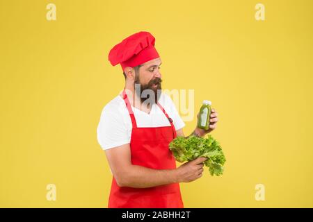 Nutrizione Vegetariana. Frullato di vitamine drink. Frullato Hipster bevanda. Bere è più facile. Succo di frutta fresco. Frullato di spremitura. Uomo Barbuto chef tenere la lattuga e bottiglia smoothie sfondo giallo. Foto Stock