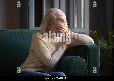 Donna anziana seduti sul divano a piangere la faccia coperta con la mano Foto Stock