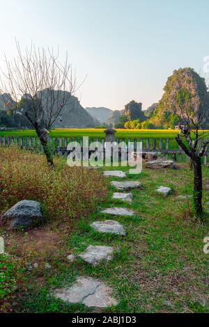 Una passerella di pietra attraverso un campo verso le montagne al tramonto a Hang Mua nel nord del Vietnam Foto Stock