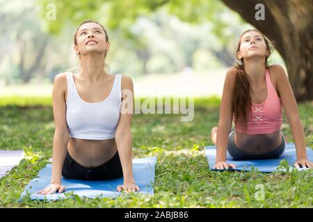 Bella ragazza adolescente modello facendo yoga di gruppo per un sano nel parco all'aperto. rivolto verso l'alto cane(Bhujangasana) postura. Foto Stock