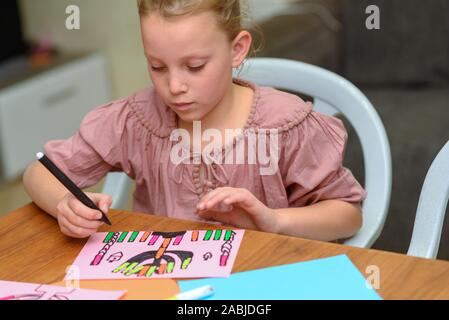 Ricamo, artigianato bambini.bambina creare un biglietto di auguri immagine della festa ebraica di Hanukkah. Kid paste stickers - candele e disegno menorah, dreidel, vasetto di olio su carta su un tavolo di legno. Foto Stock