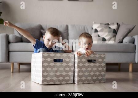 Due ragazzi seduti in una scatola di cartone in camera in appartamento Foto Stock