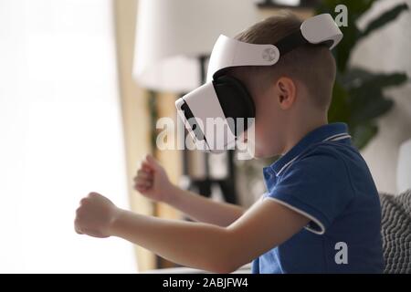 Ragazzo in realtà virtuale di occhiali e maglietta blu in piedi in appartamento su sfondo sfocato Foto Stock