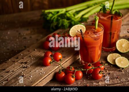 Bloody Mary cocktail in bicchieri su sfondo di legno con sale e pepe, calce, i pomodori e il sedano Foto Stock