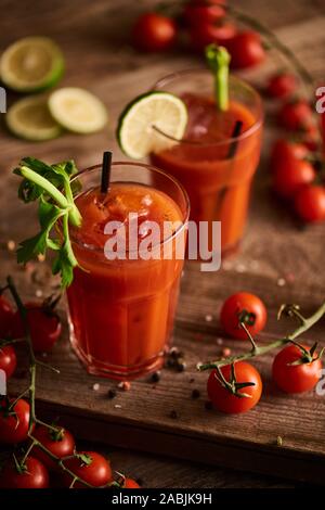 Messa a fuoco selettiva di bloody mary cocktail in bicchieri su sfondo di legno con sale e pepe, pomodori e sedano Foto Stock