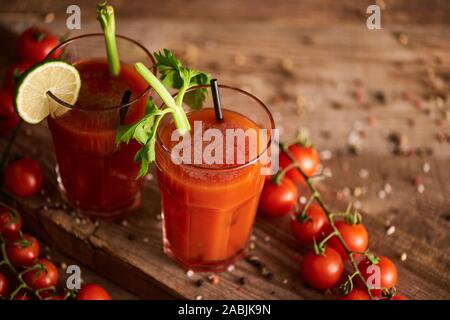 Bloody Mary cocktail in bicchieri su sfondo di legno con sale e pepe, pomodori e sedano Foto Stock