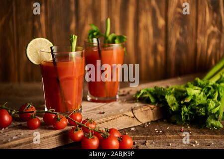 Bloody Mary cocktail in bicchieri su sfondo di legno con sale e pepe, pomodori e sedano Foto Stock