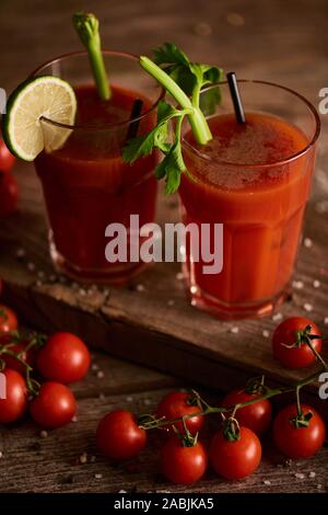 Bloody Mary cocktail in bicchieri su sfondo di legno con sale e pepe, pomodori e sedano Foto Stock