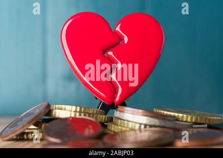 Rosso rotto il giorno di San Valentino cuore su una pila di monete in euro. Amore e Denaro problemi concetto astratto. Sfondo blu. Foto Stock